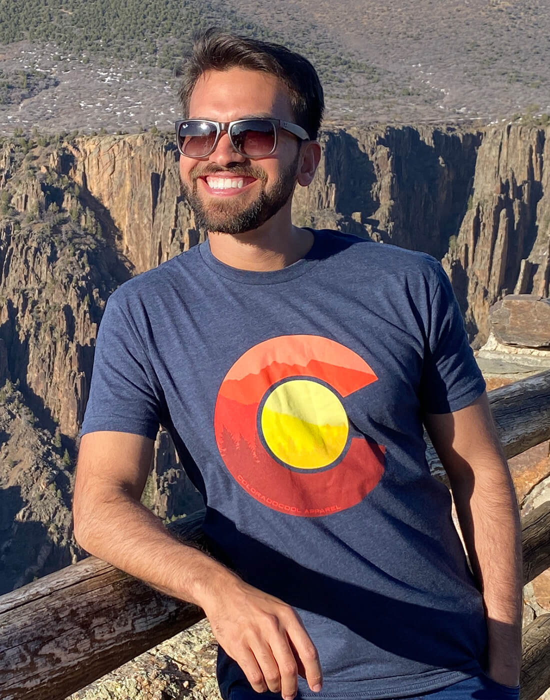 Man smiling in Colorado Flag T-Shirt in front of mountain scenery