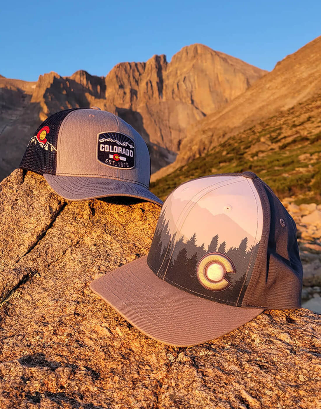 Two Colorado hats on a rock in front of a mountain peak