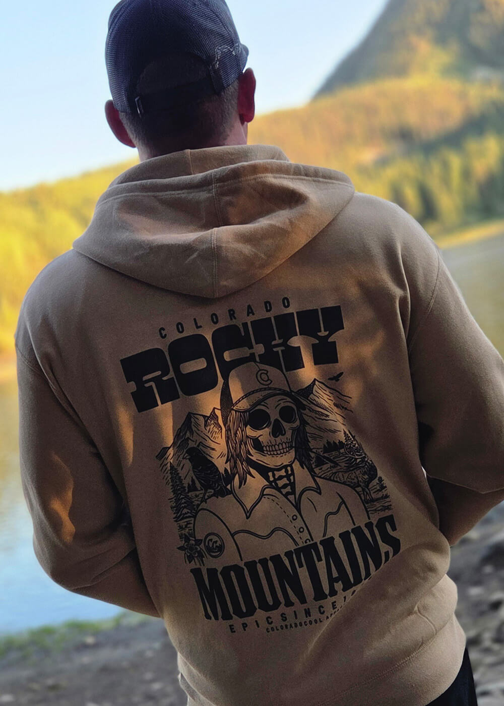 Person wearing a hoodie with 'Colorado Rocky Mountains' design, standing in a scenic outdoor setting.
